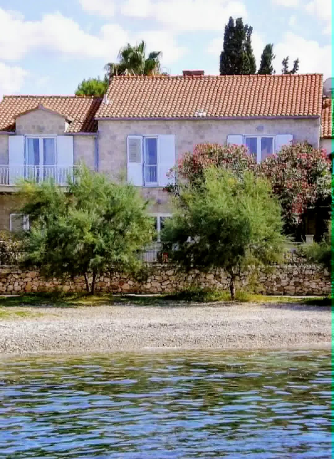 Steinfasaden på Villa Mirca med lyseblå skodder og tamariskkrans